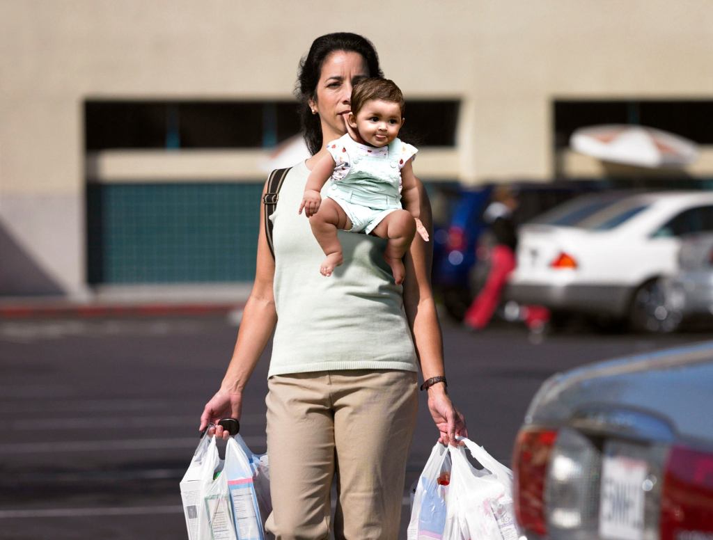 Mom With Arms Full Of Groceries Holds Baby By Scruff Of Neck With Mouth