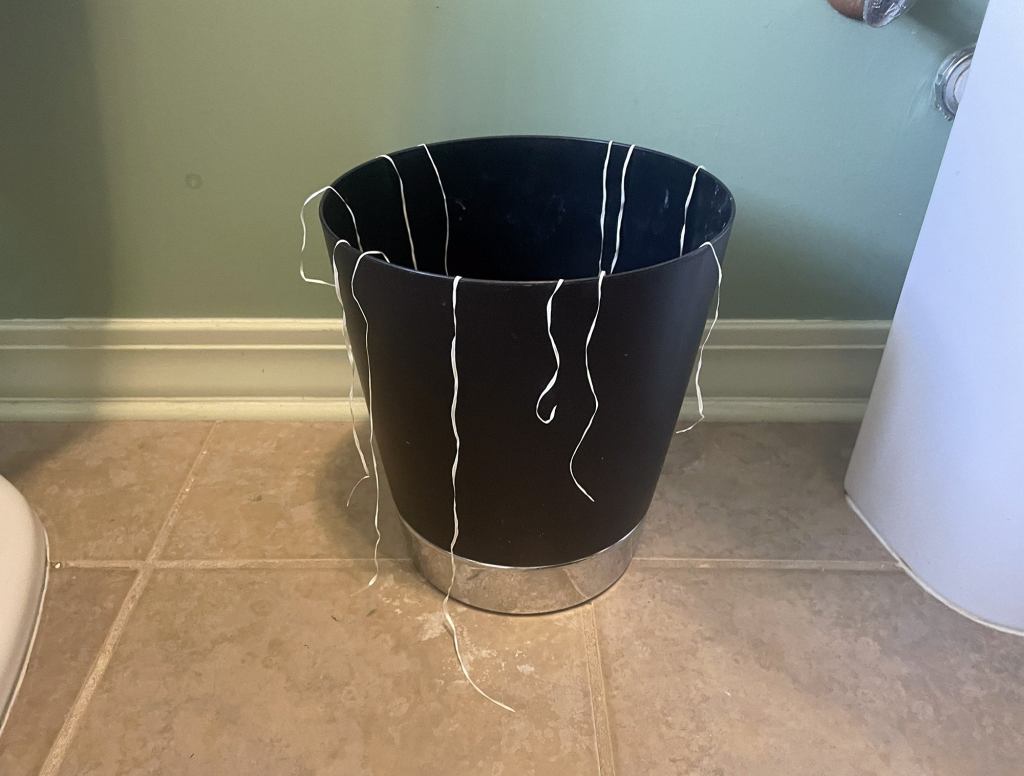 Floss Draped Around Top Of Bathroom Trash Bin Like Tinsel