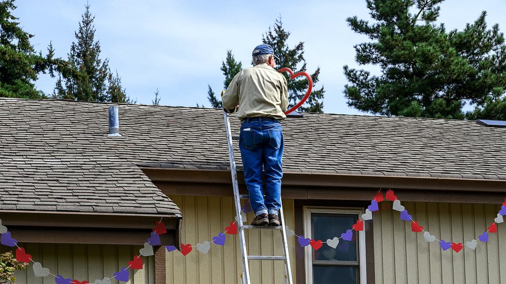 Elderly Neighbor Standing On Top Of 20-Foot Ladder To Hang Valentine’s Decorations